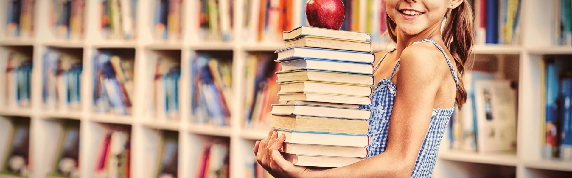 Schulmädchen hält Stapel von Büchern in der Bibliothek