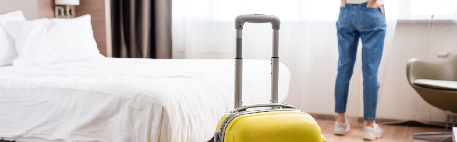 Selektiver Fokus von gelbem Gepäck in der Nähe einer Frau in einem Hotelzimmer - horizontaler Schnitt