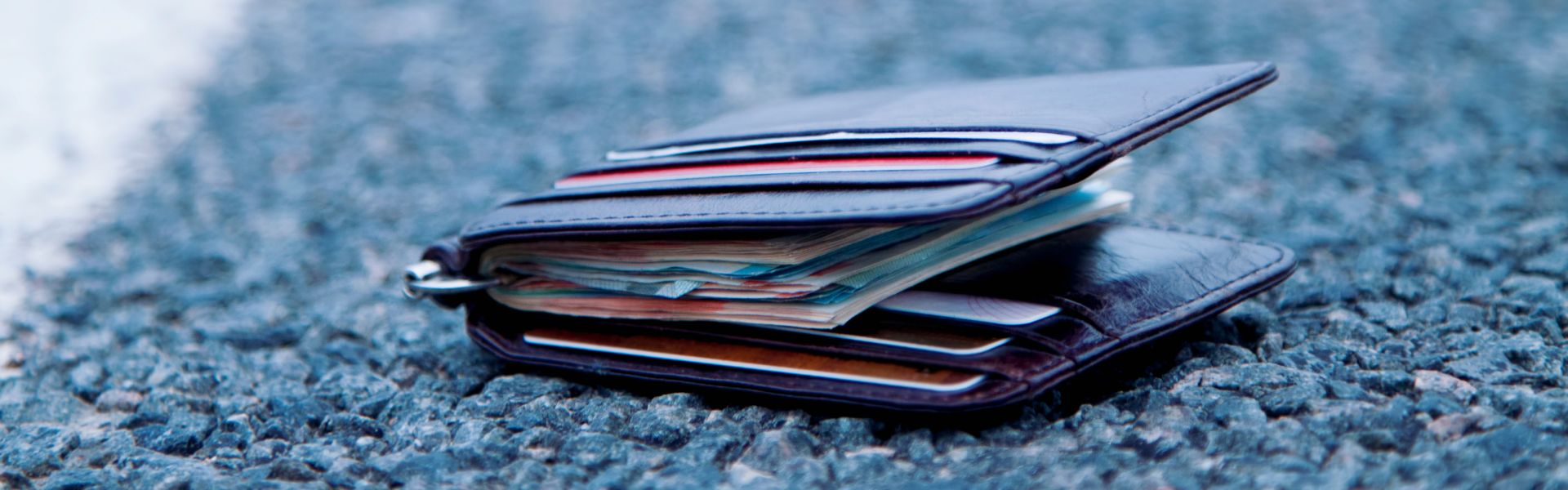 Nahaufnahme eines auf dem Gehweg liegenden Geldbeutels, gefüllt mit Banknoten unterschiedlicher Werte und verschiedener Plastikkarten.